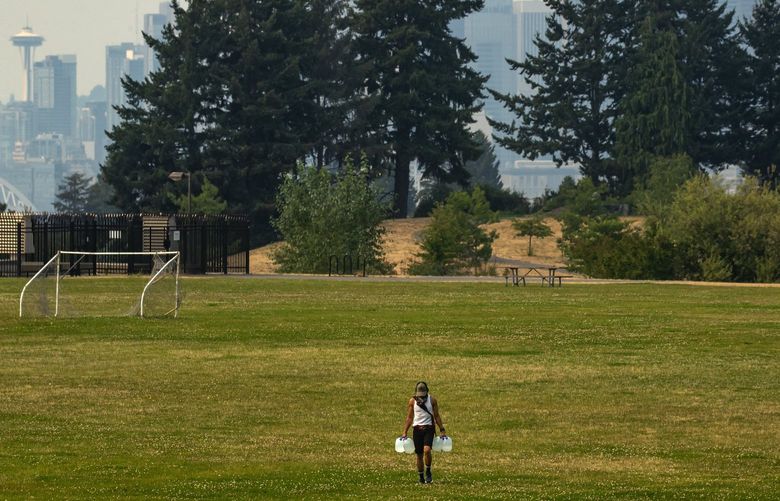 A person hauls jugs of water to their encampment after filling them up in Jefferson Park as wildfire smoke and haze hang over the region during a heat wave, with temperatures in the 90’s in Seattle Friday, August 13, 2021. 217944