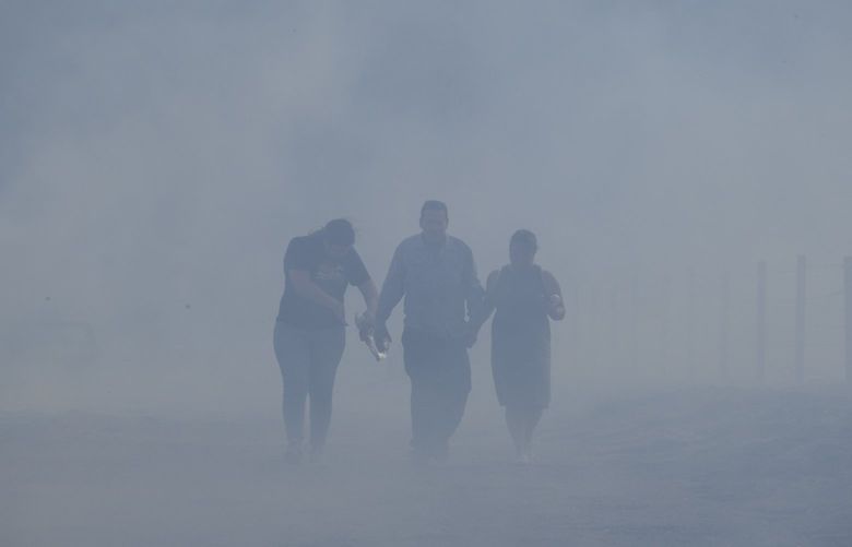Homeowners Jose Lamas, center, his wife, Maria Covarrubias, right, and his daughter Astrid Covarrubias walk through the smoke after visiting their burned-out home from the South Fire in Lytle Creek, San Bernardino County, north of Rialto, Calif., Wednesday, Aug. 25, 2021. (AP Photo/Ringo H.W. Chiu) CARC103 CARC103