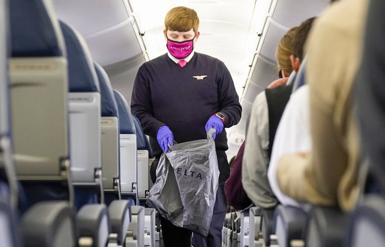 A Delta flight attendant works with a protective mask and gloves during a flight to Philadelphia, Nov. 30, 2020. (AP Photo/Paul Sancya) MIPS10