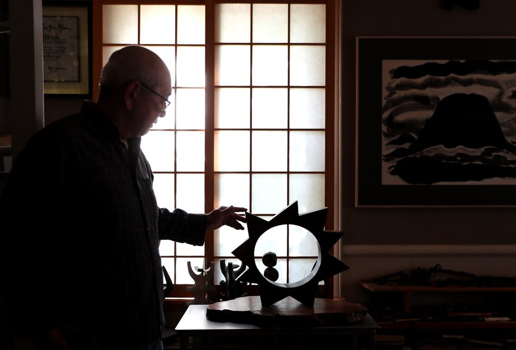 Gerard Tsutakawa touches one of his bronze pieces, 2017’s “Sun Circle,” in his study in Seattle last month. Tsutakawa is inspired by the abstraction of nature in his sculptures. (Ken Lambert / The Seattle Times)