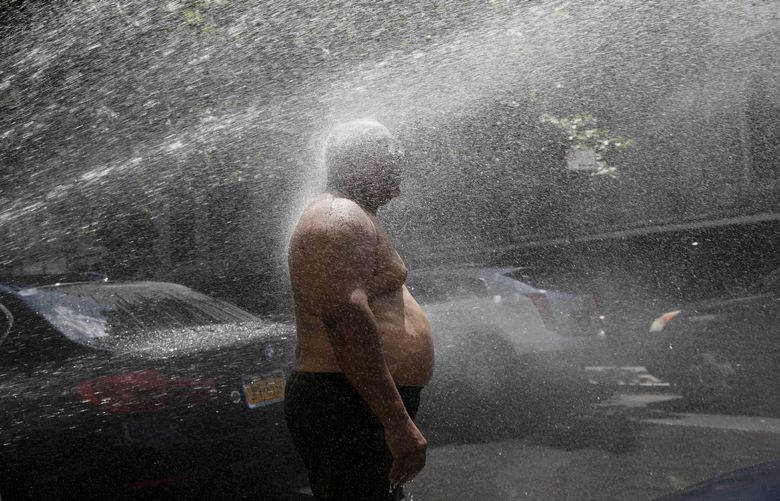 FILE – In this Tuesday, July 28, 2020 file photo, Rey Gomez cools off in the spray from a fire hydrant in New York, as the city opened more than 300 fire hydrants with sprinkler caps to help residents cool off during a heat wave. According to a study published Tuesday, May 25, 2021 in Nature Communications, during the summer of 2017 in nearly all large urban areas, people of color are exposed to more extreme urban heat than white people. (AP Photo/Mark Lennihan, File)