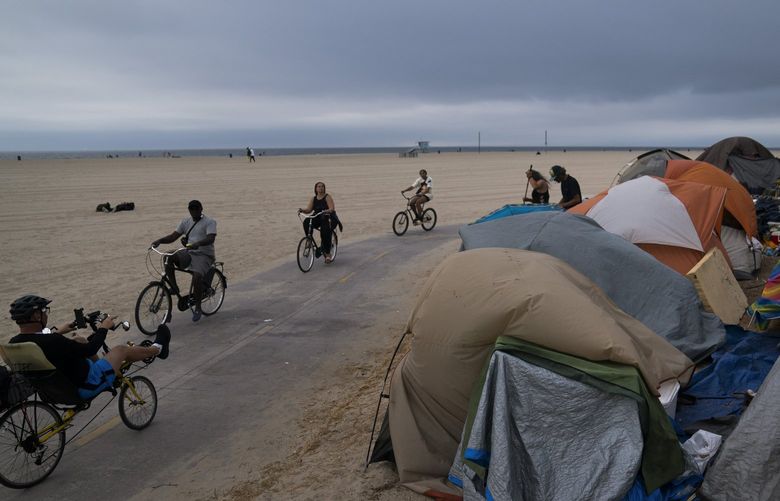 FILE – In this June 29, 2021, file photo people ride their bikes past a homeless encampment set up along the boardwalk in the Venice neighborhood of Los Angeles. The share of Americans living in poverty rose slightly as the COVID pandemic shook the economy last year, but massive relief payments pumped out by Congress eased hardship for many, the Census Bureau reported Tuesday, Sept. 14. The official poverty measure showed an increase of 1 percentage point in 2020, indicating that 11.4% of Americans were living in poverty. It was the first increase in poverty after five consecutive annual declines. (AP Photo/Jae C. Hong, File) WX101 WX101