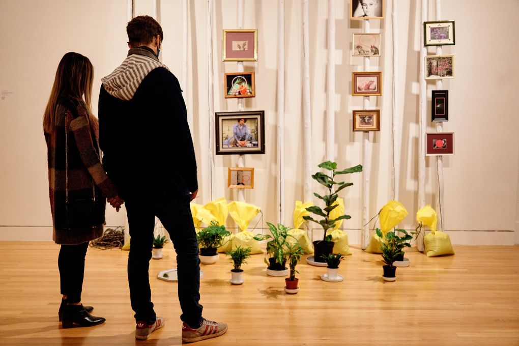Visitors to the Frye Art Museum view Duane Linklater’s “action at a distance,” created from painted teepee poles, nylon rope, plants, ceramics, sandbags, 12 framed digital prints and framed mirror. (Jonathan Vanderweit)