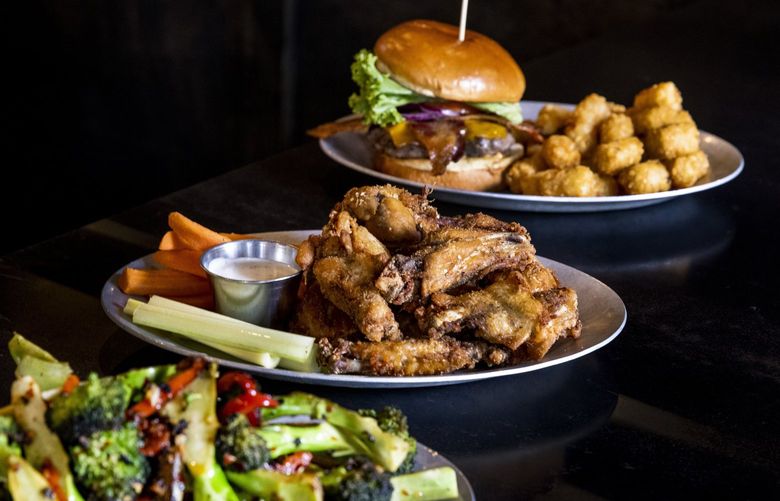 From left, broccolini, jerk dry rub chicken wings and a house burger with bacon sit on a table at Westy Roosevelt in Seattle on Wednesday, Sept. 22, 2021.  218285