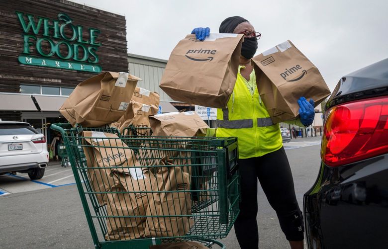 An independent contractor wearing a protective mask and gloves loads Amazon Prime grocery bags into a car outside a Whole Foods Market in Berkeley, California, U.S., on Wednesday, Oct. 7, 2020. With millions of Americans still sheltering in place and cooking their own meals, the grocery industry has been one of the few bright spots in an otherwise battered U.S. economy. Unless, that is, you are Whole Foods Market, the upscale chain acquired three years ago by Amazon.com Inc. Photographer: David Paul Morris/Bloomberg