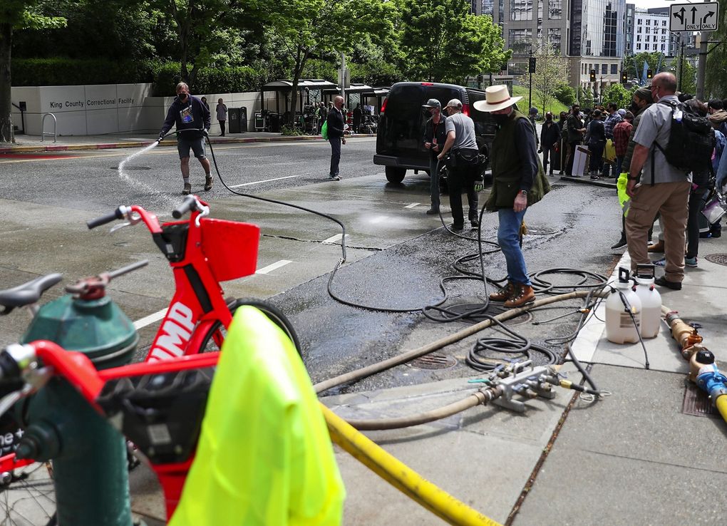 On a sunny spring day, Fifth Avenue near James Street is hosed down to make Seattle appear more stereotypically damp for cameras for the movie “Kimi.” (Ken Lambert / The Seattle Times)