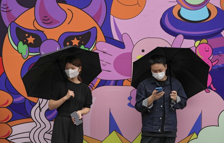 A man and a woman, both holding umbrella and wearing face masks to help curb the spread of the coronavirus stand against a wall depicting a cartoon mural in Beijing, Sunday, Sept. 12, 2021. (AP Photo/Andy Wong) XAW111 XAW111