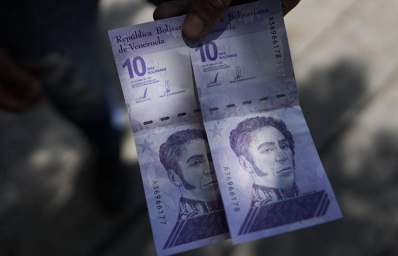 A man shows a new 10 Bolivar bank note after withdrawing it from a cash machine in Caracas, Venezuela, Friday, Oct 1, 2021. A new currency with six fewer zeros debuts Friday in Venezuela, whose currency has been made nearly worthless by years of the world’s worst inflation. The new currency tops out at 100 bolivars, a little less than $25 until inflation starts to eat away at that as well. (AP Photo/Ariana Cubillos) XAC101 XAC101