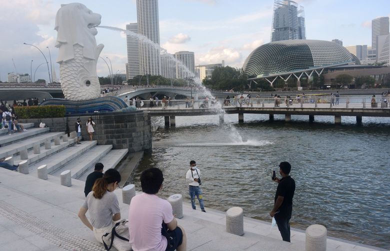 A man wearing a face mask poses for a photo with the Merlion statue in the background Sunday, Sept. 26, 2021, in Singapore. As the island nation of Singapore pursues a strategy of “living with COVID” and a gradual relaxation of pandemic restrictions, daily cases are skyrocketing and residents are growing increasingly anxious. (AP Photo/Annabelle Liang) SGP104 SGP104