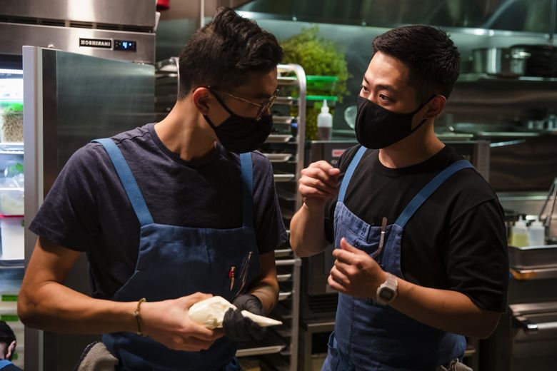 Line cooks Ben Yan, left, and Kevin Hwang talk while assembling dishes at Tomo, a new restaurant in White Center. (Bettina Hansen / The Seattle Times)
