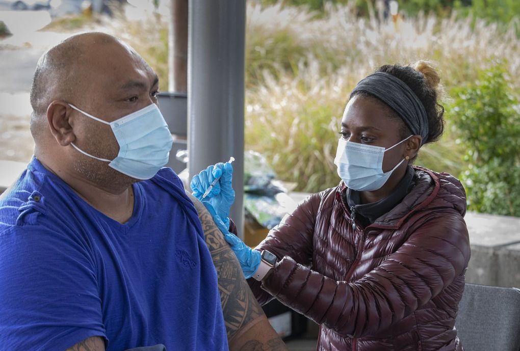 John Tausaga gets a Pfizer booster shot from nurse Betty Tesfaye on Oct. 11 at Highline College. She and others are there every Monday to provide Johnson & Johnson, Moderna and Pfizer vaccines, as well as booster shots. (Ellen M. Banner / The Seattle Times)