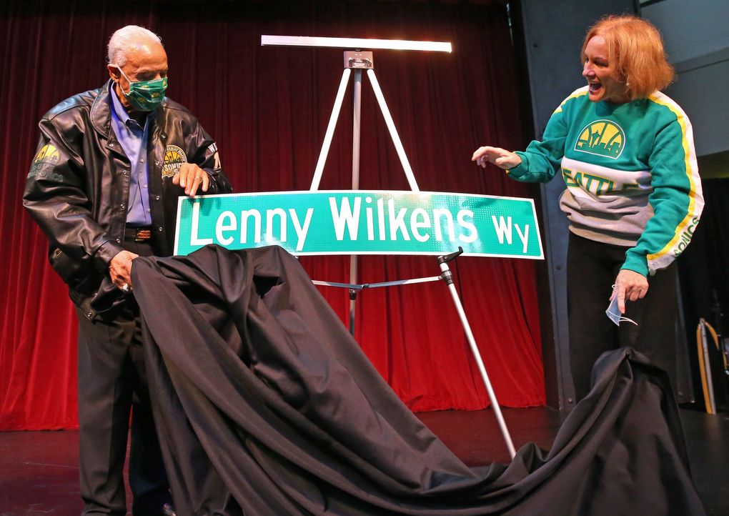 Wearing Sonics gear, Seattle mayor Jenny Durkan, right, helps Lenny Wilkens unveil a replica of “Lenny Wilkens Way” at Seattle Center Armory, Thursday, Oct. 28, 2021 in Seattle. The real signs are already up outside, but the rainy weather brought the ceremony indoors. (Ken Lambert / The Seattle Times)