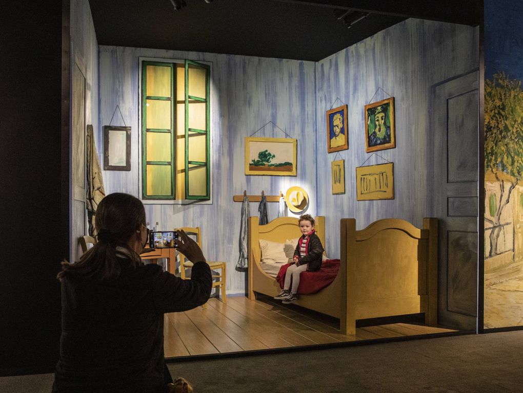 Allison Sutcliffe of Gig Harbor photographs her 3-year-old daughter Cynthia inside the diorama of Vincent Van Gogh’s bedroom that he painted many times. It’s part of the “Van Gogh: The Immersive Experience” show.(Steve Ringman / The Seattle Times)