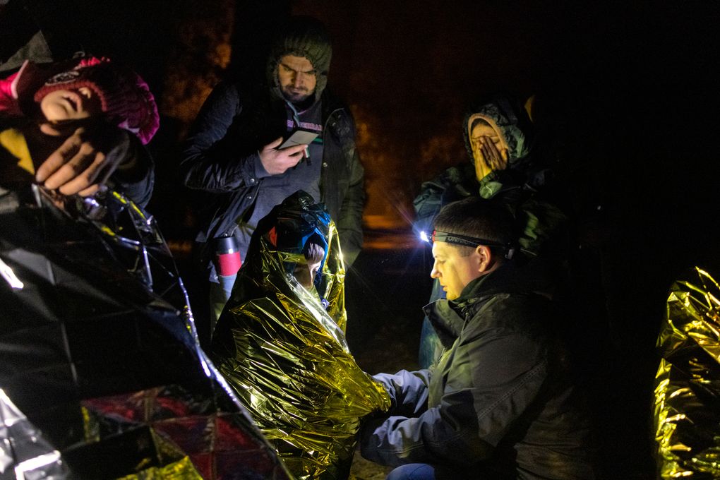Piotr Bystrianin, center, who spends his nights searching for migrants, aids a family in Poland near the border with Belarus early on Oct. 2, 2021. Bystrianin roams country roads and forest tracks in a car loaded with donated food, water, blankets and dry clothes. (Maciek Nabrdalik / The New York Times)