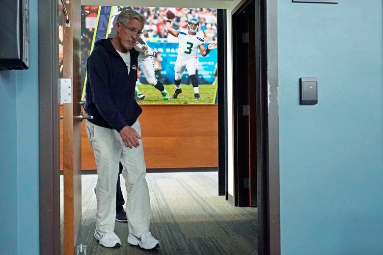 Seattle Seahawks head coach Pete Carroll walks past a photo of quarterback Russell Wilson in action as he arrives to talk to reporters before NFL football practice, Wednesday, Oct. 13, 2021, in Renton, Wash. Wilson is out with a finger injury and backup quarterback Geno Smith is scheduled to start Sunday on the road against the Pittsburgh Steelers in an NFL football game. (AP Photo/Ted S. Warren)