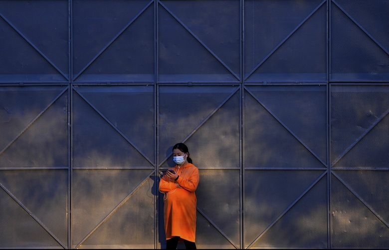 A pregnant woman wearing a face mask to help curb the spread of the coronavirus uses her smartphone as she sunbathes next to the steel frames at a construction site in Beijing, Wednesday, Oct. 27, 2021. (AP Photo/Andy Wong) ASIA506 ASIA506