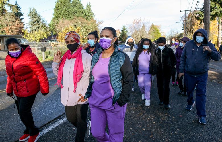 Yeshiemebet Desta (left with the pink scarf) and Mister Beneberu (right with the purple mask) join their coworkers Monday morning as they walk back into Cascade Behavioral Health Hospital, after more than three months of striking.