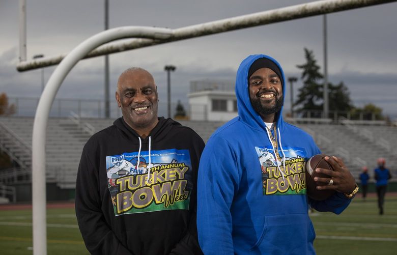 Charles E. Sampson (l) and his nephew Cortez Charles stand near the goal post at Rainier Beach High School in Seattle Friday, November 12, 2021.   In 1959 Sampson started a neighborhood touch football game in the South at the age of ten and he and his friends and family played every year until several of them went into the military in the 60s. In 1977, Sampson and his wife moved to Seattle and restarted the tradition between the Sampsons and the Mannings (his wife’s family) and grew the tradition to include a canned food drive and more families and friends, even city officials. In the late 1990’s the tradition fizzled out as the family got older. Sampson’s nephew Cortez Charles restarted the tradition in the 2000s and it is now an annual multi-day program called the Turkey Bowl that invites youth to volunteer then cap off a week of service with a flag football game.  They now hand out around 2,000 hygiene and warming kits to shelters in Seattle and Federal Way and to tiny home villages all over Seattle.  The kits contain hats, gloves, socks, hand sanitizer, soap, tooth brushes, tooth paste, deodorant and hand warmers.  They also hand out around 3,000 sandwiches .  To help, donations can be made on the Cash app at $fam0508.  For more information, go to:  www.trusttheeprocess.org.
 218765