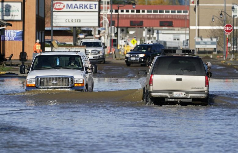 Cars drive through floodwaters Wednesday, Nov. 17, 2021, in Sumas, Wash. People in the small city of Sumas are assessing damage from flooding that hit an estimated three quarters of homes in the community near the Canadian border. (AP Photo/Elaine Thompson) NVJL216 NVJL216