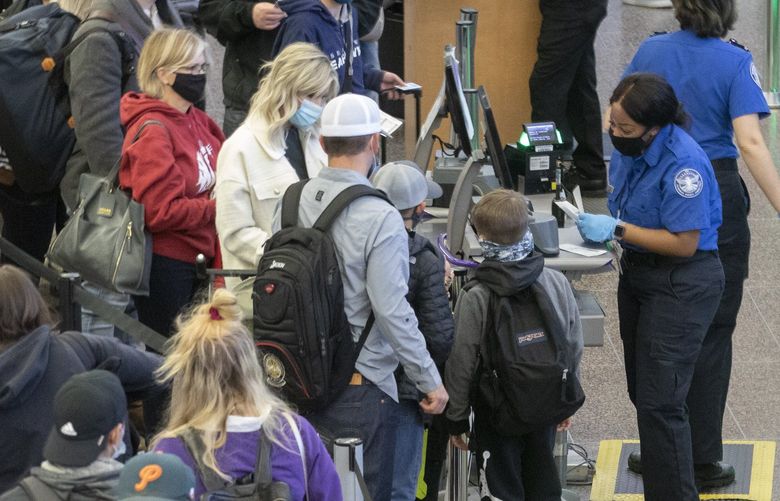 A TSA agent checks the I. D. of a passenger in the security line at check point two at Seattle-Tacoma International Airport (SEA) early Friday morning, November 19, 2021. Crowds early Friday morning were relatively small but that will change soon. 1.5 million travelers are expected to go through the airport from Thursday, November 18 through Monday, November 29. That is 150% more travelers than the airport served in 2020. It is about 88% of pre-pandemic travel in 2019. The parking garage was packed. 218872