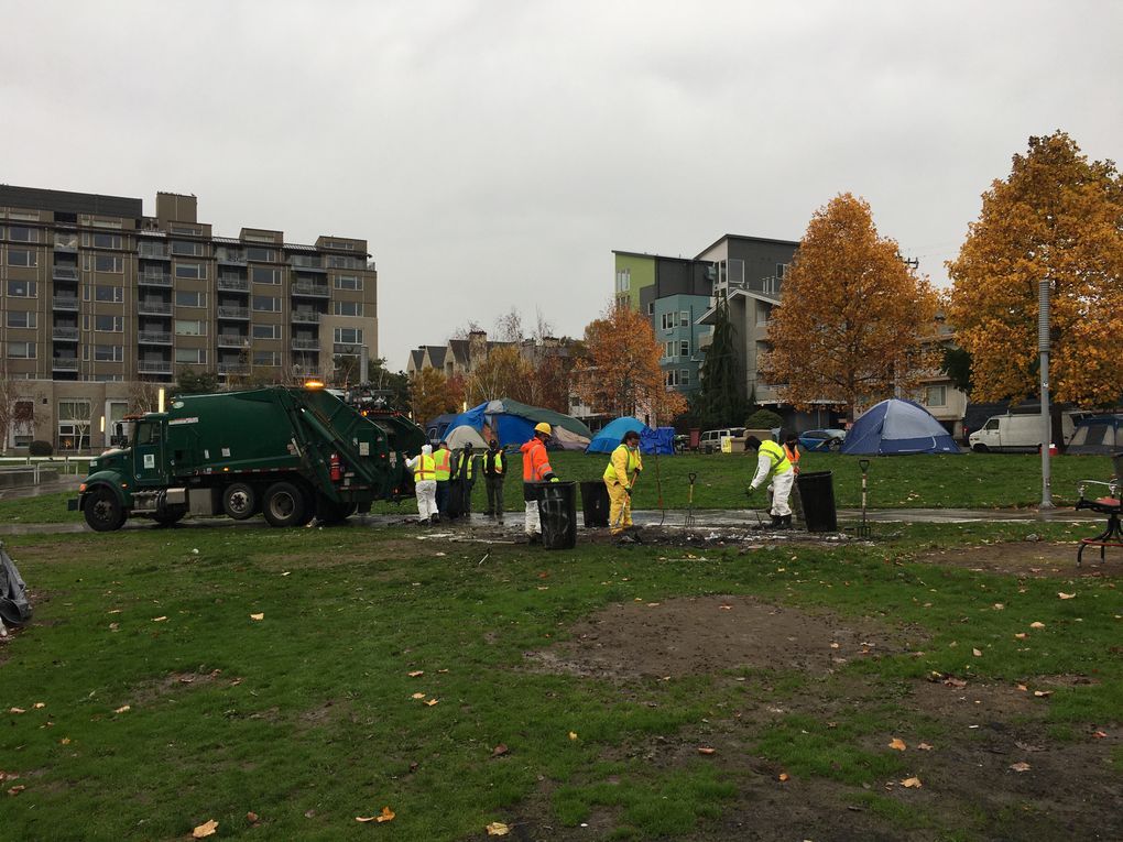 A city crew cleaned up the charred remnants of a tent fire Tuesday at an encampment in Ballard Commons Park. (Lewis Kamb / The Seattle Times)