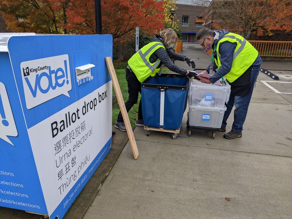 King County election drivers Paula Eisenrich, left, and Robb Brennecke fill a plastic ballot bin with sealed ballots shortly after 9 a.m. at the NewHolly Neighborhood Campus dropbox in Beacon Hill. This was their third stop on a day that will last until 11 p.m. They said they’ll be watching the weather because they need to make sure ballots don’t get soaked. “We move very quickly,” Brennecke said. (Jenn Smith / The Seattle Times)