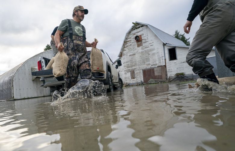 Tw men place sandbags to try and stop the rising floodwaters following heavy rain in Barrowtown near Abbotsford, British Columbia, Friday, Nov. 19, 2021. (Jonathan Hayward/The Canadian Press via AP) JOHV120 JOHV120