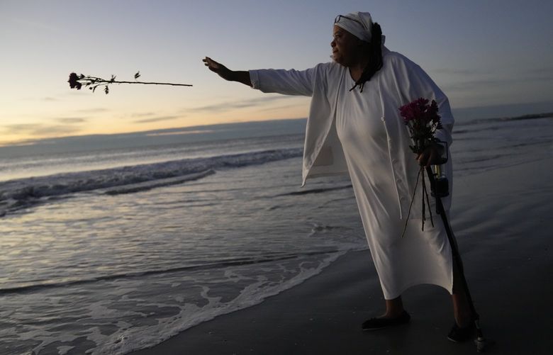 Gullah Geechee community elder Sandra Boyd, also known as “Mama Sasa,” throws a flower into the Atlantic Ocean during a dawn ceremony she held to honor the African ancestors who made the Middle Passage, either perishing en route or surviving to build new lives under the shackles of slavery, in Hunting Island State Park, on Hunting Island, S.C., Monday, Nov. 1, 2021. The dawn event kicked off a week-long community effort organized by Boyd, to clean up and beautify cemeteries on St. Helena Island, some of which are so overgrown and hidden on old plantation lands that locating them has proved a challenge. (AP Photo/Rebecca Blackwell) SCRB312 SCRB312