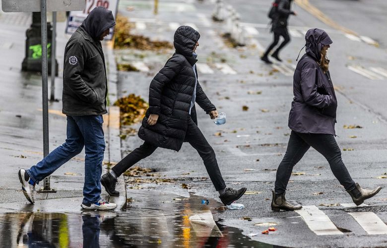 Chloe Weiss, center, stretches over a large puddle as she walks with her friends Tegan Brand, right, and Clint Ratliff in the Pioneer Square neighborhood in Seattle during a rain shower on Saturday, Nov. 6, 2021. LO 218745