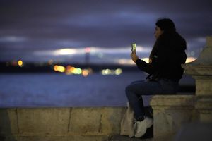 A young woman speaks on the phone by the Tagus river in Lisbon, Portugal, as night falls Monday, Dec. 6, 2021. (Armando Franca / The Associated Press)
