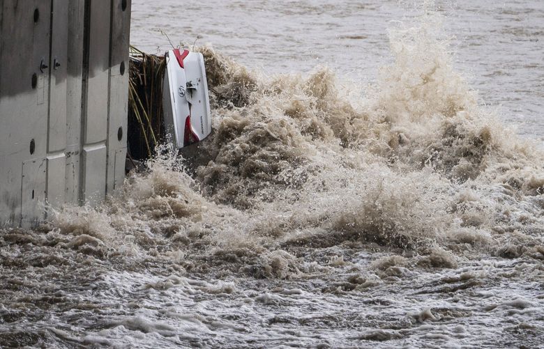 A submerged vehicle is wedged against a bridge pillar in the surging Los Angeles River making it difficult for firefighters to access it on Tuesday, Dec. 14, 2021 in Los Angeles. The vehicle was spotted in the river before dawn. Rain is drenching Southern California as a powerful storm slides down the state, snarling traffic and raising the threat of mudslides in areas scarred by wildfires. (AP Photo/Damian Dovarganes) CADD201 CADD201