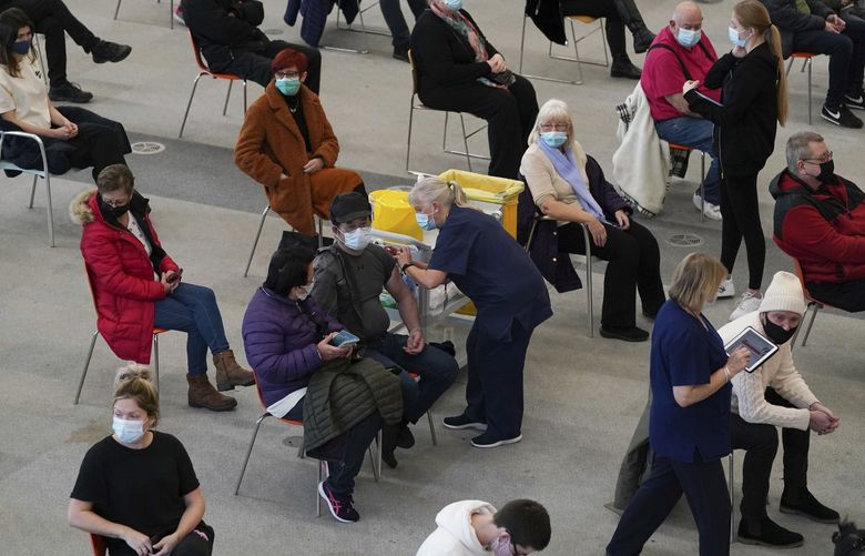 People receive a dose of a coronavirus vaccine, at a COVID-19 vaccination centre in Ramsgate, England, Tuesday, Dec. 14, 2021. Long lines have formed for booster shots across England as the U.K. government urged all adults to protect themselves against the omicron variant. (Gareth Fuller/PA via AP) AMB805 AMB805