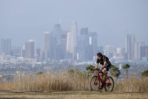 6 月 16 日，在洛杉矶，一名骑自行车的人以洛杉矶市中心为背景。 根据 2021 年 12 月 17 日星期五发布的数据，加利福尼亚州的主要人口中心洛杉矶和旧金山湾区首次在同一年失去人口。（Ringo HW Chiu / 美联社）