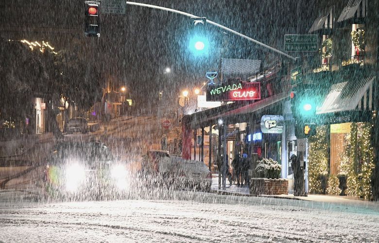 FILE – Motorists navigate downtown Grass Valley, Calif.’s roadways during an early morning snowfall, on, Dec. 14, 2021. Forecasters said Saturday, Dec. 18, 2021, that another round of widespread rain and heavy snow in the mountains is shaping up for recently drenched California and much of Nevada in the coming week and could create hazards for holiday travelers. (Elias Funez/The Union via AP, File) CAGRA501 CAGRA501