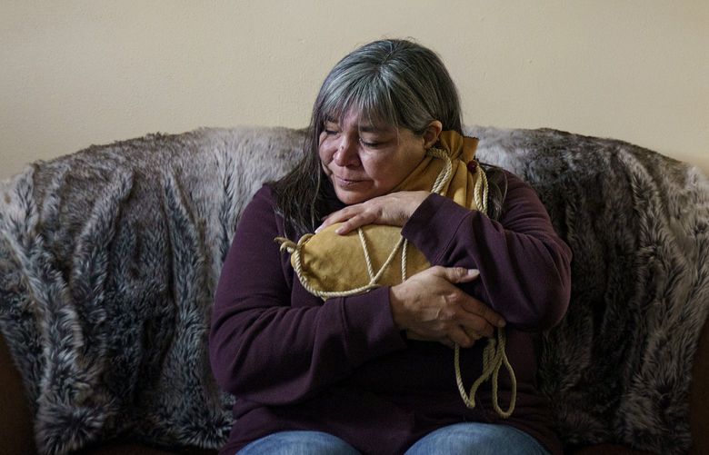 Rachel Taylor clutches a buckskin satchel filled with the ashes of her son, Kyle “Little Crow” Domrese, pictured at right, who died of an overdose, as she sits in the home they shared in Bemidji, Minn., Wednesday, Nov. 17, 2021. Just weeks remained until the anniversary of the day she opened his bedroom door and found her son face-down on his bed, one of more than 100,000 Americans lost in a year to overdoses as the COVID-19 pandemic aggravated America’s addiction disaster. The death rate from drug overdoses for Native Americans has surpassed white people and is now the highest in the nation. (AP Photo/David Goldman) MNDG201 MNDG201