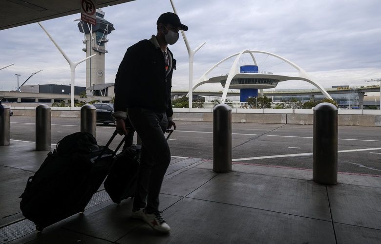 A holiday traveler wearing a face mask arrives at the Los Angeles International Airport in Los Angeles, Wednesday, Dec. 22, 2021. (AP Photo/Ringo H.W. Chiu) CARC108 CARC108