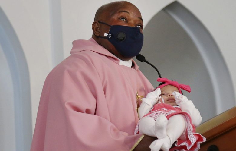 The Rev. Athanasius Abanulo introduces newborn, Nathalia Perez, to the congregation at Immaculate Conception Catholic Church on Sunday, Dec. 12, 2021, in Wedowee, Ala. Originally from Nigeria, Abanulo is one of numerous international clergy helping ease a U.S. priest shortage by serving in Catholic dioceses across the country. (AP Photo/Jessie Wardarski) nyjw213 nyjw213
