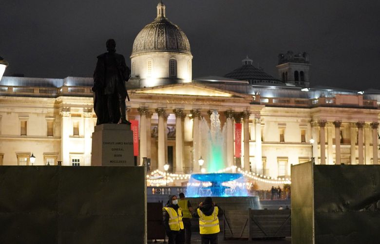 Security guards stand next to a boarding that has been erected around the parameters of Trafalgar Square, in London, Thursday, Dec. 30, 2021. British Prime Minister Boris Johnson has resisted implementing new restrictions on business and social interactions during the holiday season, instead emphasizing an expanded vaccine booster program to control the spread of omicron. (Jonathan Brady/PA via AP) LOPH402 LOPH402