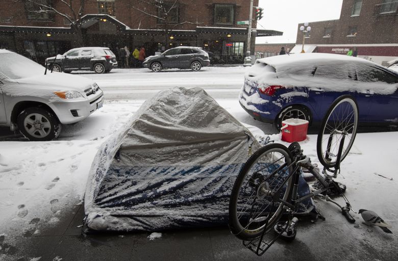 A tent gets partial shelter from the snow, halfway under a building’s awning along First Avenue near Pike Place Market in downtown Seattle on Sunday. (Ken Lambert / The Seattle Times)