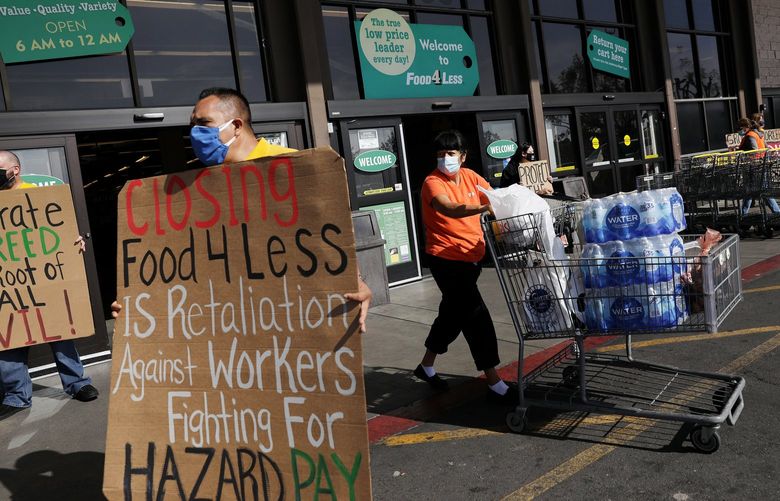 A shopper passes by a group holding signs in support for Food 4 Less workers at the grocery store  in North Long Beach on Wednesday, Feb. 3, 2021. (Christina House/Los Angeles Times/TNS)
