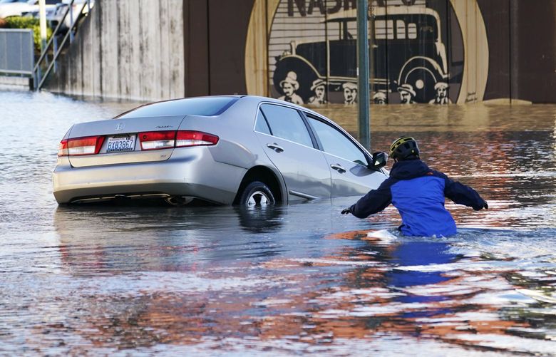 FILE – Kenneth Warner races into the water to help rescue the driver of a car that went into the flooded Nooksack River, Tuesday, Nov. 16, 2021, in Ferndale, Wash. Winter has started out weird in the United States. It’s been flip flop weather in much of the country with the Pacific Northwest getting record rainfall and Denver and the Rockies still haven’t seen their first significant snowfall of the season. (AP Photo/Elaine Thompson, File) NYMV301 NYMV301