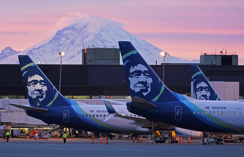 FILE – Alaska Airlines planes are parked at gates with Mount Rainier in the background at sunrise, March 1, 2021, at Seattle-Tacoma International Airport in Seattle. Alaska Airlines said Thursday, Jan. 6, 2022, it will trim its schedule by about 10% for the rest of January at it deals with â€œunprecedentedâ€ numbers of employees calling in sick during the current COVID-19 surge. (AP Photo/Ted S. Warren, File) NYDD201 NYDD201