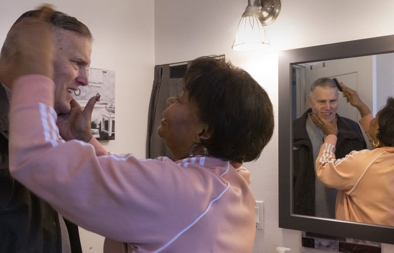 Angela Petersen combs her husband Chris’s hair in the bathroom of the Tukwila home they share before the two head out to attend a women’s basketball game at Seattle University where their daughter Lexi is an assistant coach Monday, January 10, 2022.
Angela is a caregiver for her husband who suffers with dementia. They live off disability and social security.  She quit her job to become a full-time caregiver for him because paid caregiving was too expensive.  As the legislature debates WA Cares Fund, unpaid caregiving and long-term care is taking a toll on women. 219282