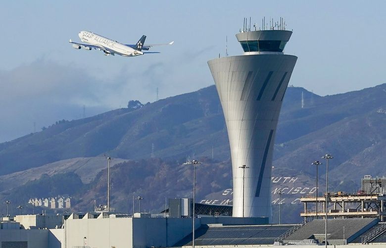 FILE – In this Nov. 24, 2020, file photo, a plane takes off behind the air traffic control tower at San Francisco International Airport in San Francisco. (AP Photo/Jeff Chiu,File) 