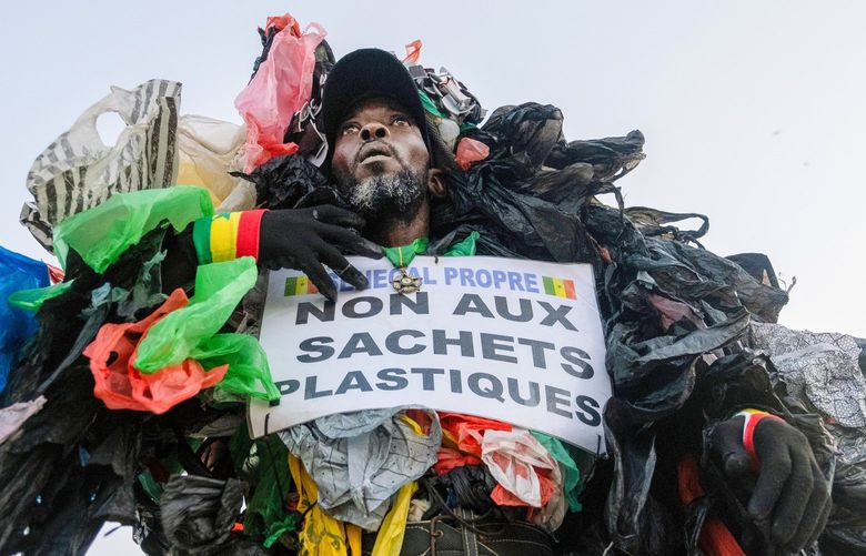 Modou Fall, who works to educate fellow Senegalase residents about the dangers of plastic trash, holds a sign reading â€œno to plastic bagsâ€ as he makes his case at the annual marathon in Dakar, Senegal, on Nov. 21, 2021. Dressed head to toe in plastic, Modou Fall is a familiar sight in Dakar. (Ricci Shryock/The New York Times) XNYT40