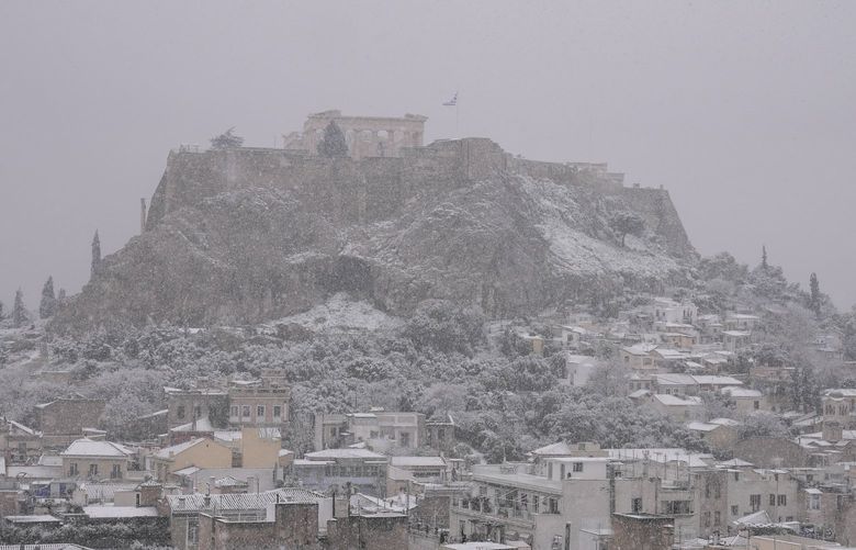 The city of Athens with the Parthenon temple atop the ancient Acropolis hill is covered with snow during a snowfall, on Monday, Jan. 24, 2022.The wave of bad weather hitting Greece is forecast to continue through Tuesday, and has seen snow falling even on some islands. Authorities have warned the public to avoid all but essential outdoor movement, and several major roads and highways are passable only with snow chains. (AP Photo/Thanassis Stavrakis) XPG118 XPG118