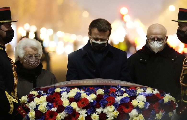 French President Emmanuel Macron, center, flanked by Auschwitz concentration camp survivor Esther Senot, second left, and Bergen-Belsen concentration camp survivor Victor Perahia, second right, lays flowers at the Tomb of the Unknown Soldier under the Arc de Triomphe to mark the International Holocaust Remembrance Day, Thursday, Jan. 27, 2022 in Paris. . Holocaust survivors and politicians warned about the resurgence of antisemitism and Holocaust denial as the world remembered Nazi atrocities and commemorated the 77th anniversary of the liberation of the Auschwitz concentration camp on Thursday. (AP Photo/Thibault Camus, Pool) PAR130 PAR130