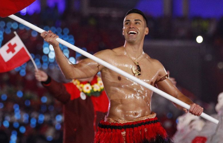 FILE – In this Feb. 9, 2018, file photo, Peta Taufatofua carries a flag of Tonga during the opening ceremony of the 2018 Winter Olympics in Pyeongchang, South Korea, Friday, Feb. 9, 2018. Taufatofua decided to leave his shirt on Tuesday, June 23, 2020 when he led a group of 23 fellow Olympians in a home workout video to help celebrate Olympic Day across 20 time zones. (AP Photo/Jae C. Hong, File)