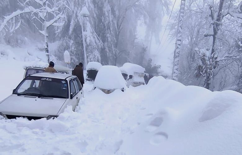 In this photo provided by the Inter Services Public Relations, people walk past vehicles trapped in a heavy snowfall-hit area in Murree, some 28 miles (45 kilometers) north of the capital of Islamabad, Pakistan, Saturday, Jan. 8, 2022. Temperatures fell to minus 8 degrees Celsius (17.6 Fahrenheit) amid heavy snowfall at Pakistan’s mountain resort town of Murree overnight, killing multiple people who were stuck in their vehicles, officials said Saturday. (Inter Services Public Relations via AP) ISL105 ISL105