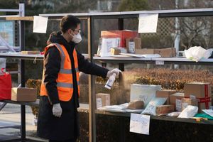 In this photo released by Xinhua News Agency, a staff member disinfects parcels at a community under close-off management where a locally transmitted COVID-19 case was found in Haidian in Beijing, China on Tuesday, Jan. 18, 2022. (Ren Chao/Xinhua via AP)
